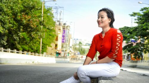 Asian Woman in Red Top Sitting on Urban Roadside 4K Desktop Wallpaper