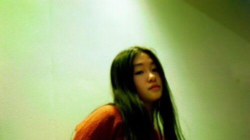 Aesthetic Portrait of a Young Asian Girl in an Orange Sweater 4K Wallpaper