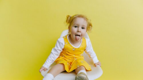 Cute Little Girl Sticking Out Tongue Against Yellow Background Desktop Wallpaper