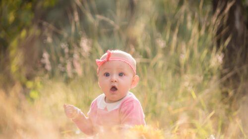 Cute Baby Girl with Surprised Expression in Golden Meadow 4K Wallpaper