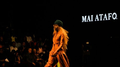 Fashion Runway Model in Orange Jumpsuit and Green Hat 4K Wallpaper