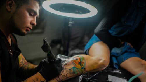 Tattoo Artist Working on a Vibrant Frog Leg Tattoo 4K Wallpaper