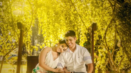 Happy Couple Sitting on Wooden Swing Under Sunlit Trees 4K Wallpaper