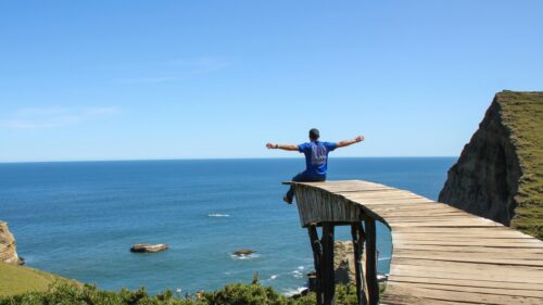 Man Sitting on Wooden Cliff Overlook Ocean View 4K Wallpaper