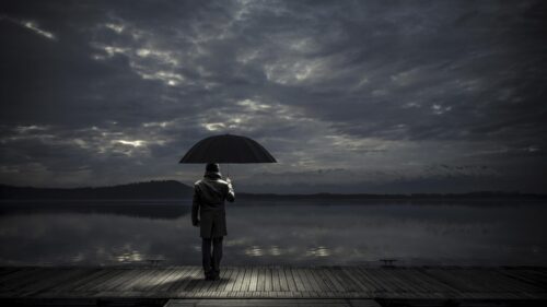 Melancholic Man Holding Umbrella on Wooden Pier at Twilight PC Wallpaper