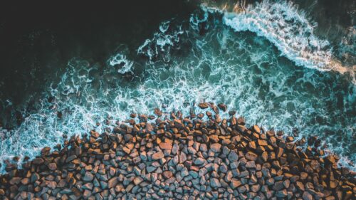 Stunning Aerial View of Crashing Ocean Waves on Rocky Shoreline PC Wallpaper