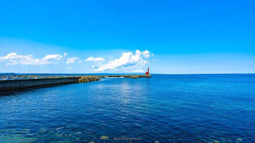 Stunning Seascape with Vibrant Red Lighthouse Under Clear Blue Sky PC Wallpaper