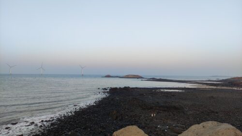 Serene Seascape with Offshore Wind Turbines and Rocky Shoreline PC Wallpaper