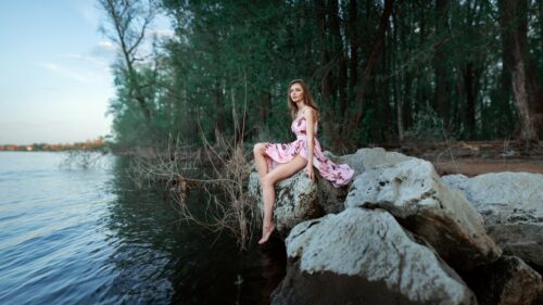 Stunning Woman in Pink Floral Dress Sitting on Rocks by the Lake PC Wallpaper