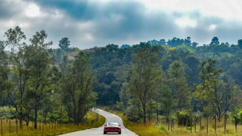 Classic Red Sports Car Driving on Scenic Country Road Desktop Wallpaper