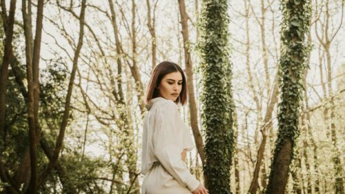Woman in White Outfit Standing in Sunlit Forest 4K Desktop Wallpaper
