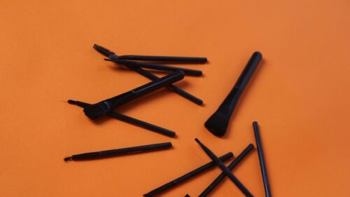 Minimalist Black Makeup Brushes on Vibrant Orange Background 4K Wallpaper