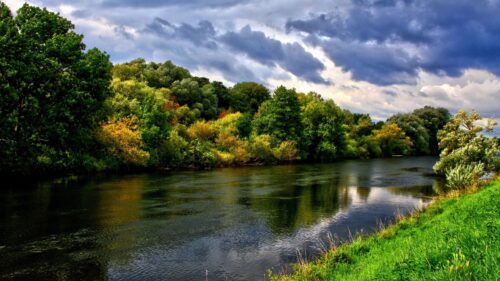 Serene River Landscape with Lush Green Trees and Stormy Clouds 4K Wallpaper
