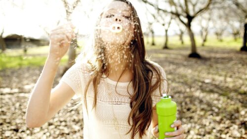 Beautiful Young Woman Blowing Bubbles in Sunlit Orchard PC Wallpaper
