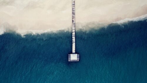 Minimalist Aerial View of a Wooden Pier Extending into the Deep Blue Ocean 4K Wallpaper