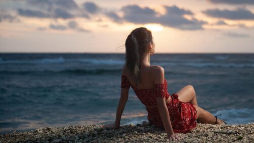 Woman Sitting on Pebble Beach at Sunset 4K Wallpaper