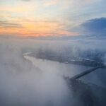 Cityscape Shrouded in Fog at Sunrise with River and Bridge