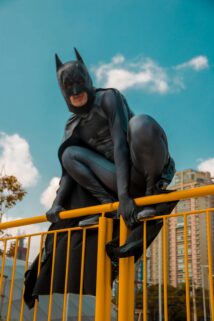 A Costumed Man Poses Dynamically As A Superhero On A Yellow City Fence During The Day – Free 4K HD Download