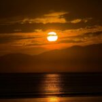 Golden Sunset Over Calm Ocean And Distant Mountains