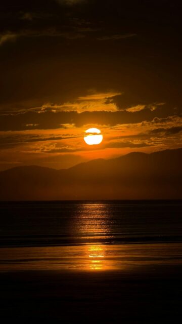 Golden Sunset Over Calm Ocean And Distant Mountains