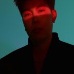 Man with Red Light Across Face on Teal Background