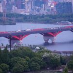 Urban Oasis: Red Bridge Over River with City Skyline