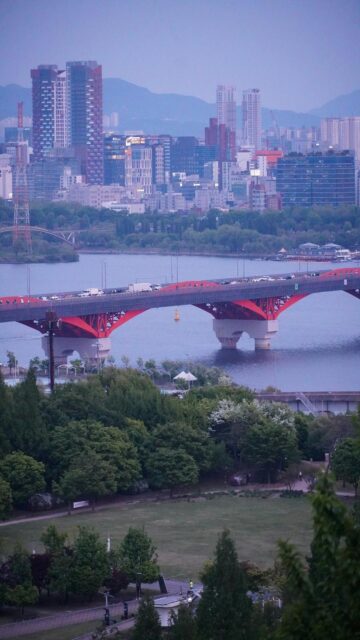 Urban Oasis: Red Bridge Over River with City Skyline