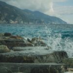 Nature's Harmony: Waves on Rocky Shore with Majestic Mountains