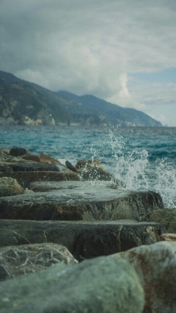 Nature's Harmony: Waves on Rocky Shore with Majestic Mountains