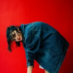Woman in Denim Jacket Bends Over Red Backdrop