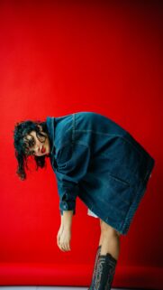 Woman in Denim Jacket Bends Over Red Backdrop
