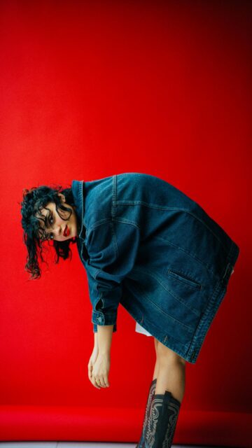 Woman in Denim Jacket Bends Over Red Backdrop