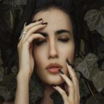 Ethereal Moment: Woman with Eyes Closed Surrounded by Dark Leaves