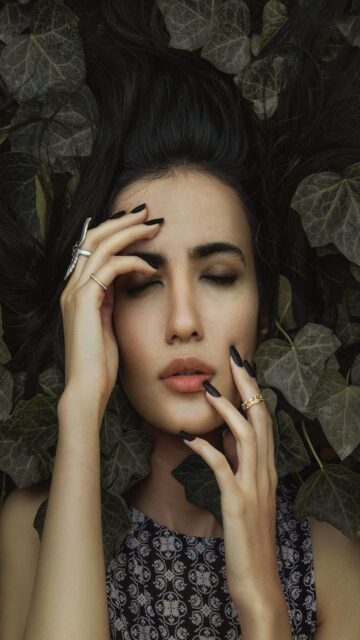 Ethereal Moment: Woman with Eyes Closed Surrounded by Dark Leaves