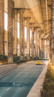 Stunning Yellow Taxi Driving Under Massive Concrete Highway Overpass Wallpaper