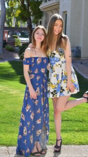 Two Beautiful Young Women in Floral Summer Dresses Standing on a Sunny Green Lawn Wallpaper