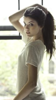 Stunning Portrait of a Young Woman Adjusting Her Hair by the Window High Quality Mobile Wallpaper
