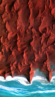 Stunning Aerial View of Red Sand Dunes Meeting the Turquoise Ocean Mobile Wallpaper