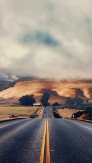 Scenic Open Road Through Golden Hills and Moody Clouds Mobile Wallpaper