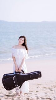 Elegant Woman in White Dress Holding Guitar Case on Beach Wallpaper