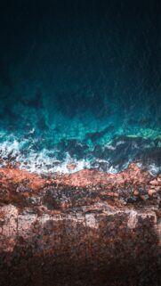 Stunning Aerial View of Turquoise Ocean Waves Crashing Against Rocky Cliffs Wallpaper