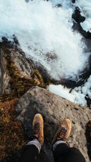 First-Person Perspective of Hiking Boots Over a Rushing Waterfall Wallpaper