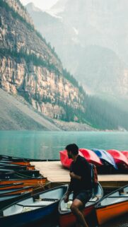 Man Standing by Canoes at Moraine Lake Adventure Phone Wallpaper