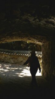 Person Walking Through Stone Tunnel to Garden Path Wallpaper