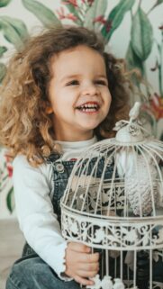 Adorable Curly Haired Toddler Girl Holding Birdcage Phone Wallpaper