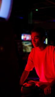 Young Man Playing Arcade Game with Neon Red Lighting Mobile Wallpaper