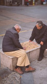 Elderly Men Playing Chinese Chess Outdoor Moment Wallpaper