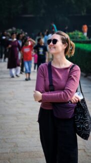 Smiling Woman in Maroon Top Standing on Stone Pathway Mobile Wallpaper