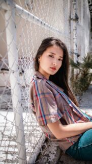 Stunning Asian Woman in Plaid Shirt Leaning Against Fence Wallpaper