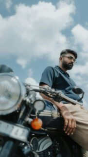 Stylish Man Leaning on Vintage Motorcycle Under Blue Sky Wallpaper